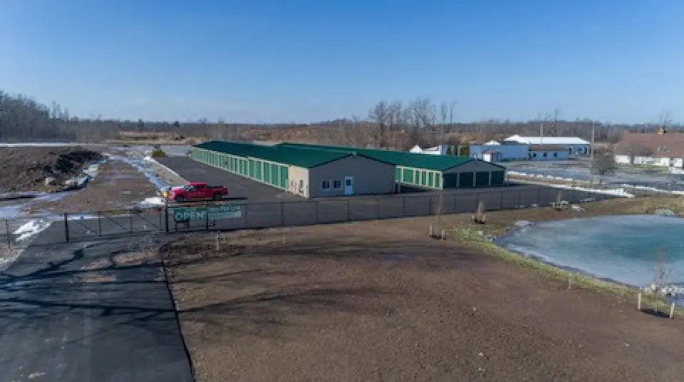 A fenced storage facility with green roofs, a red truck, and some snow on the ground.