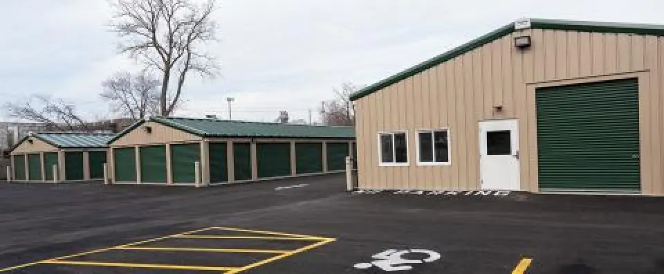 Row of storage unit buildings with green doors and accessible parking spaces in front.