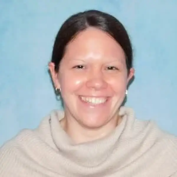 Smiling woman with brown hair and a beige sweater against a blue background.