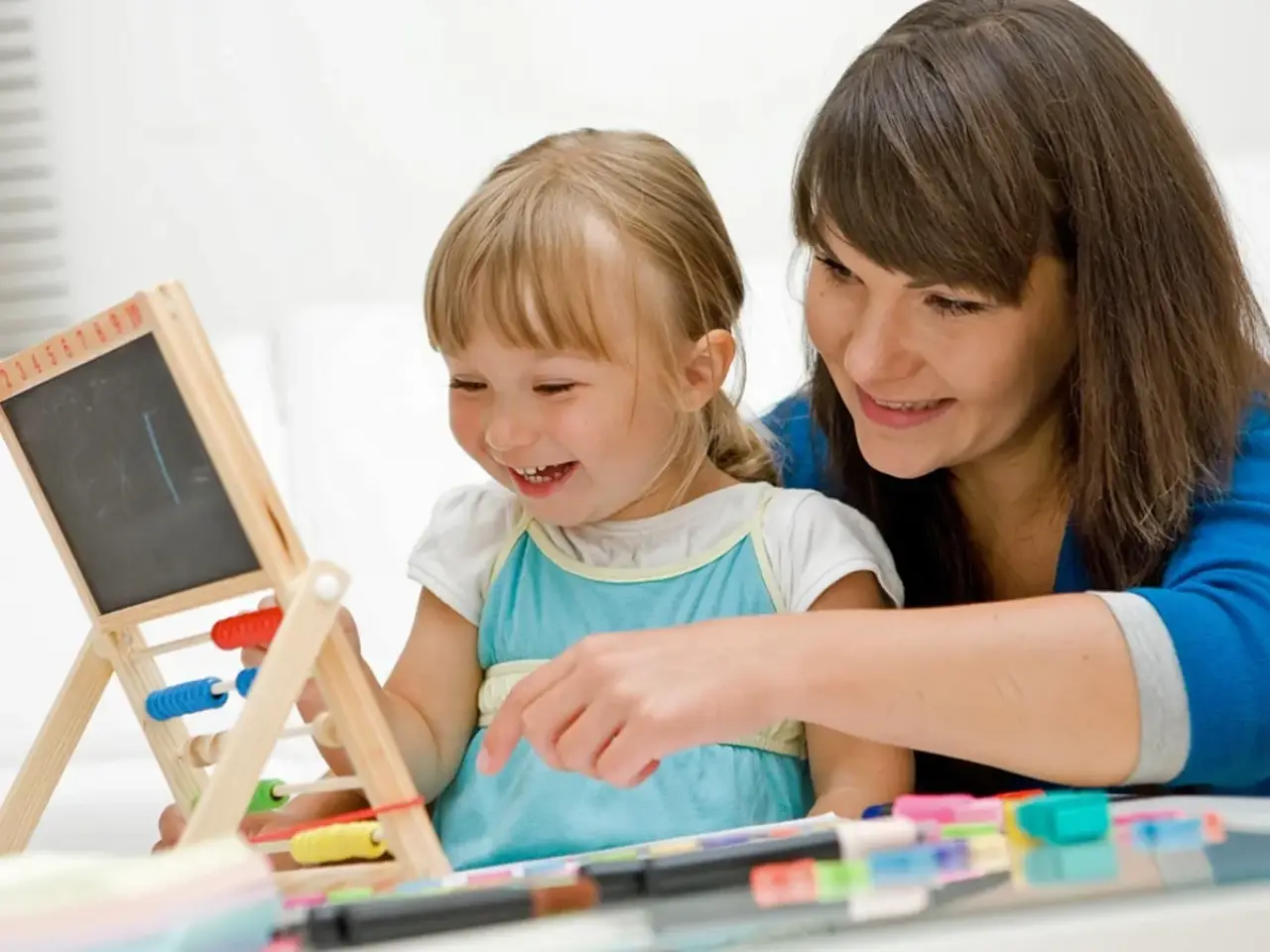 A woman and a young girl smile and play together with an abacus and chalkboard.