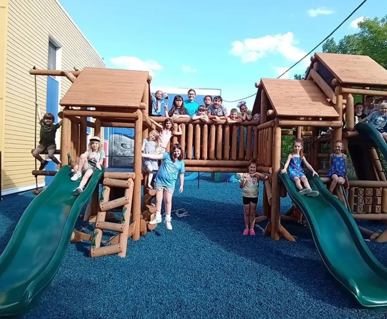 Children on a wooden playground set smiling at the camera.
