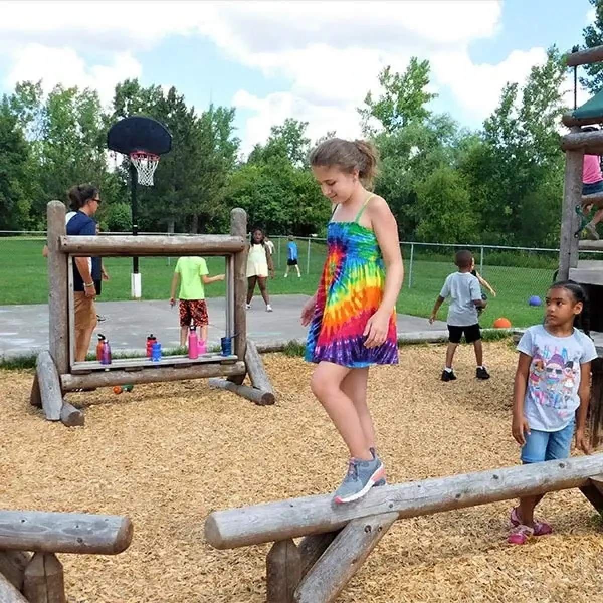 Children play on wooden playground equipment outside, with trees and a basketball hoop in the background.