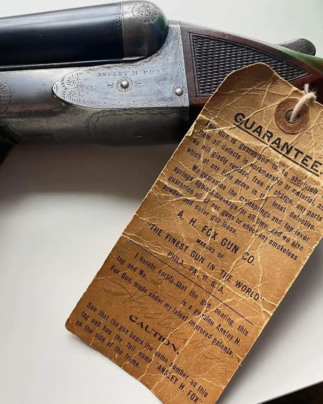 Vintage shotgun with detailed engraving and a worn guarantee tag attached.