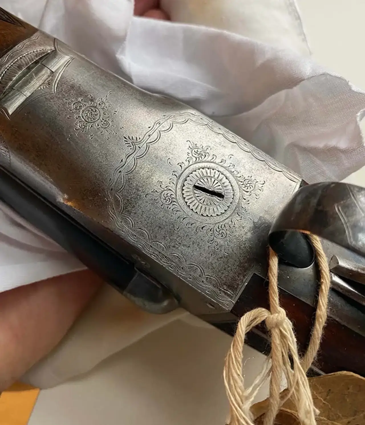 Ornate metal gun with intricate designs, held with a white cloth and a tag attached.