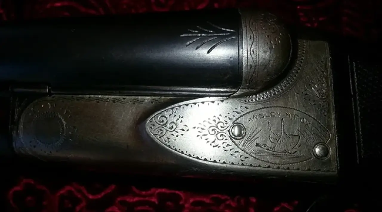 Close-up of engraved shotgun with floral design on a red patterned background.