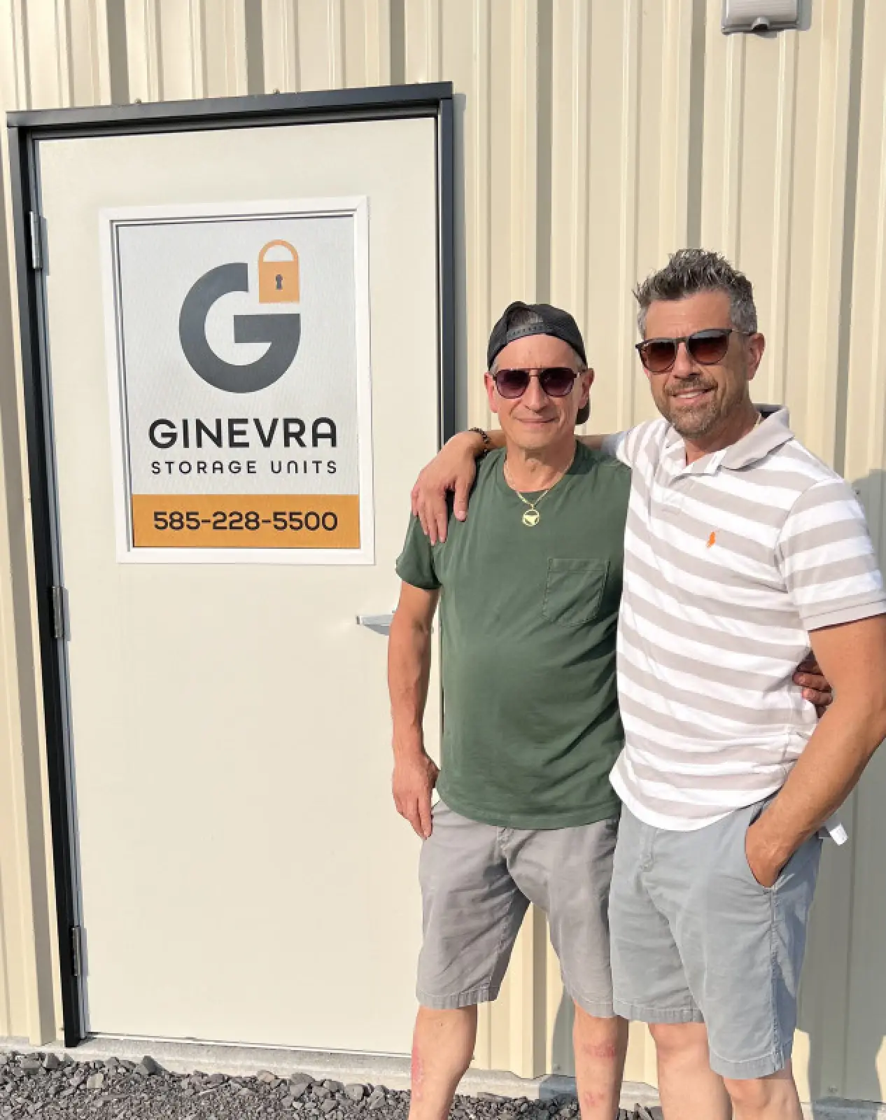 two men posing with arm over shoulder in front of building