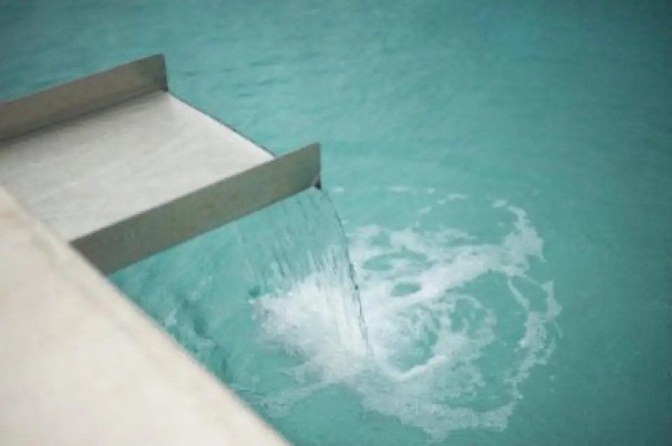 water flows from a spout into a clear blue swimming pool creating ripples and bubbles below