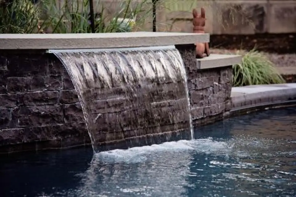 Sheer descent waterfall flowing from a stone wall into a pool.