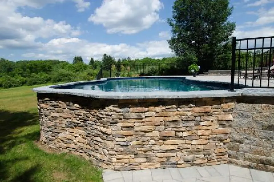 Raised backyard pool with stone wall and countryside view.