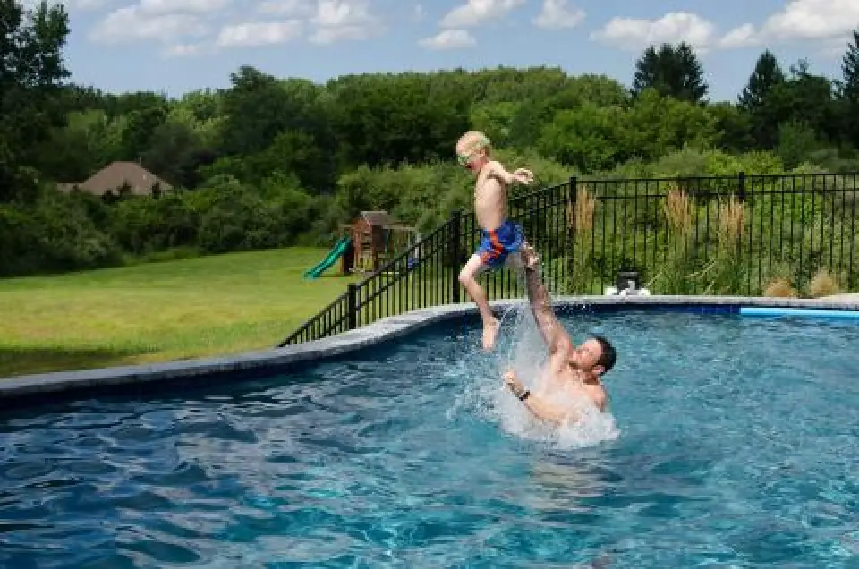 Man lifting a child above a backyard swimming pool.