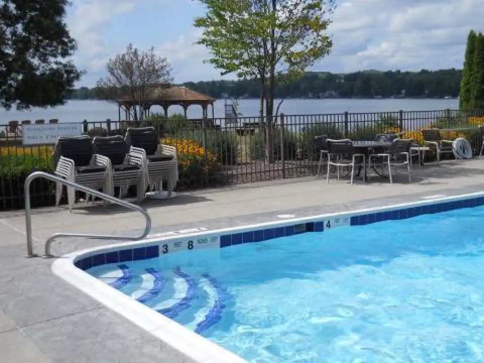 Outdoor pool with blue water, poolside chairs, a lakeside view, and a dock with a gazebo.