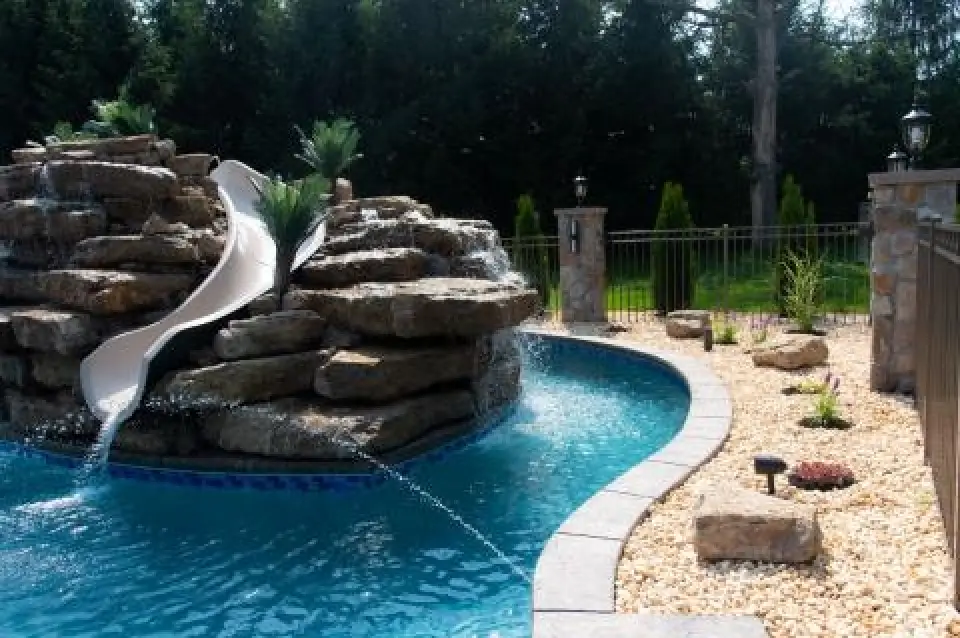 Curved residential pool with a rock waterfall and white slide.