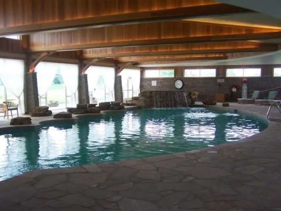 Indoor pool with stone deck, lounge chairs, large windows, and a small waterfall feature.