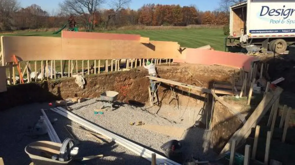 A worker builds a pool foundation with boards and gravel at an outdoor construction site.