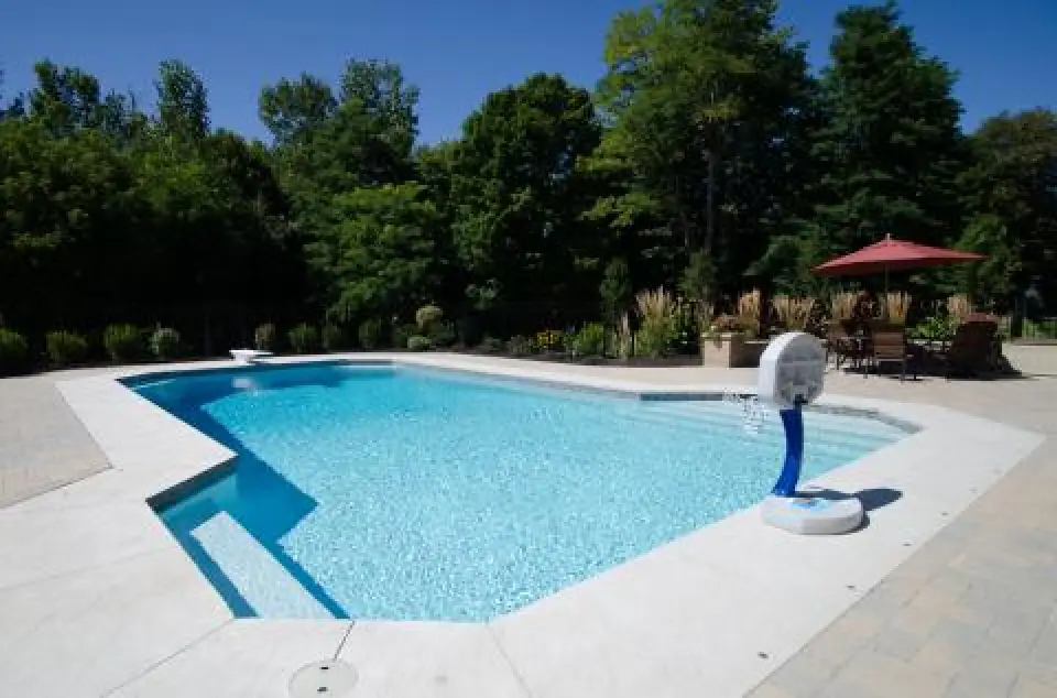 A backyard swimming pool with clear water, surrounded by trees and patio furniture.