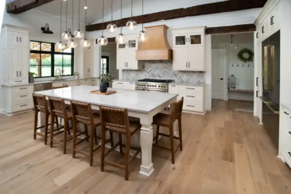 Bright white kitchen with large island, woven stools, and pendant lights.