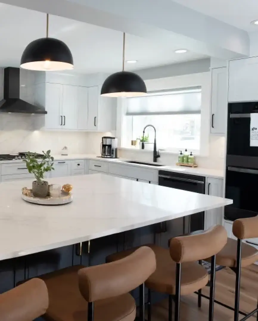 Modern kitchen with white countertops, dark island, and pendant lights.
