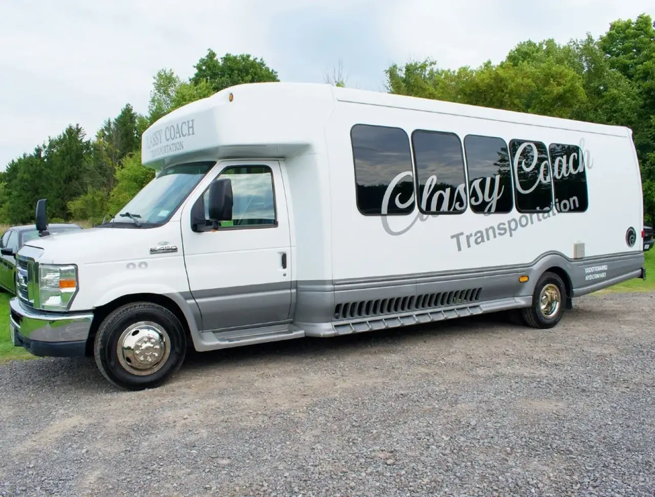Classy Coach Transportation white limo bus parked on a gravel lot.