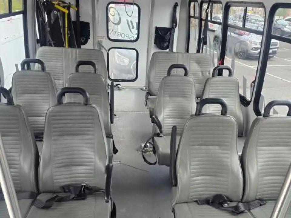 Wheelchair-accessible bus interior with gray passenger seats and a wide center aisle.