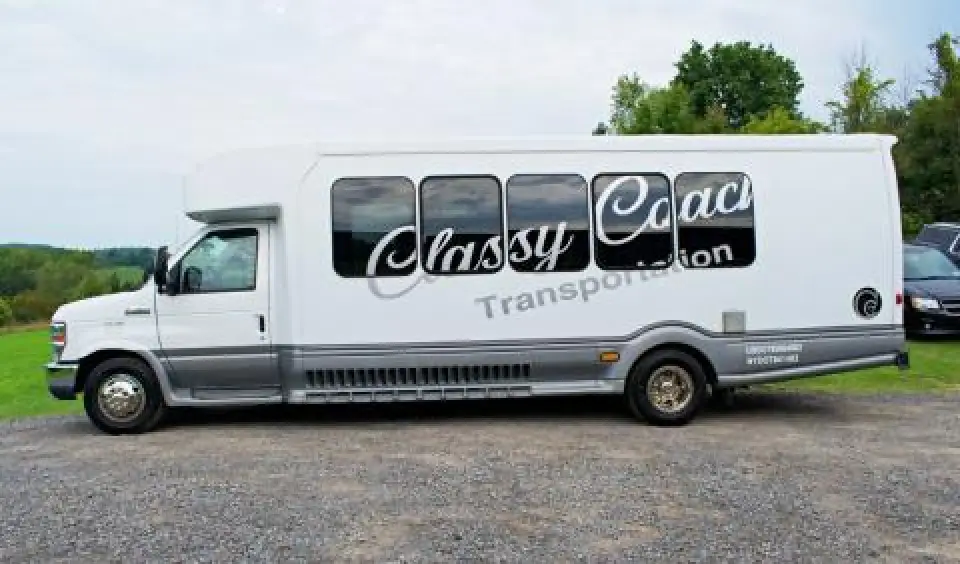 White Classy Coach shuttle bus parked on a gravel lot.