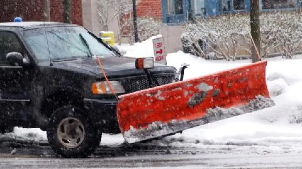 dark colored truck with red plow diving through the steet