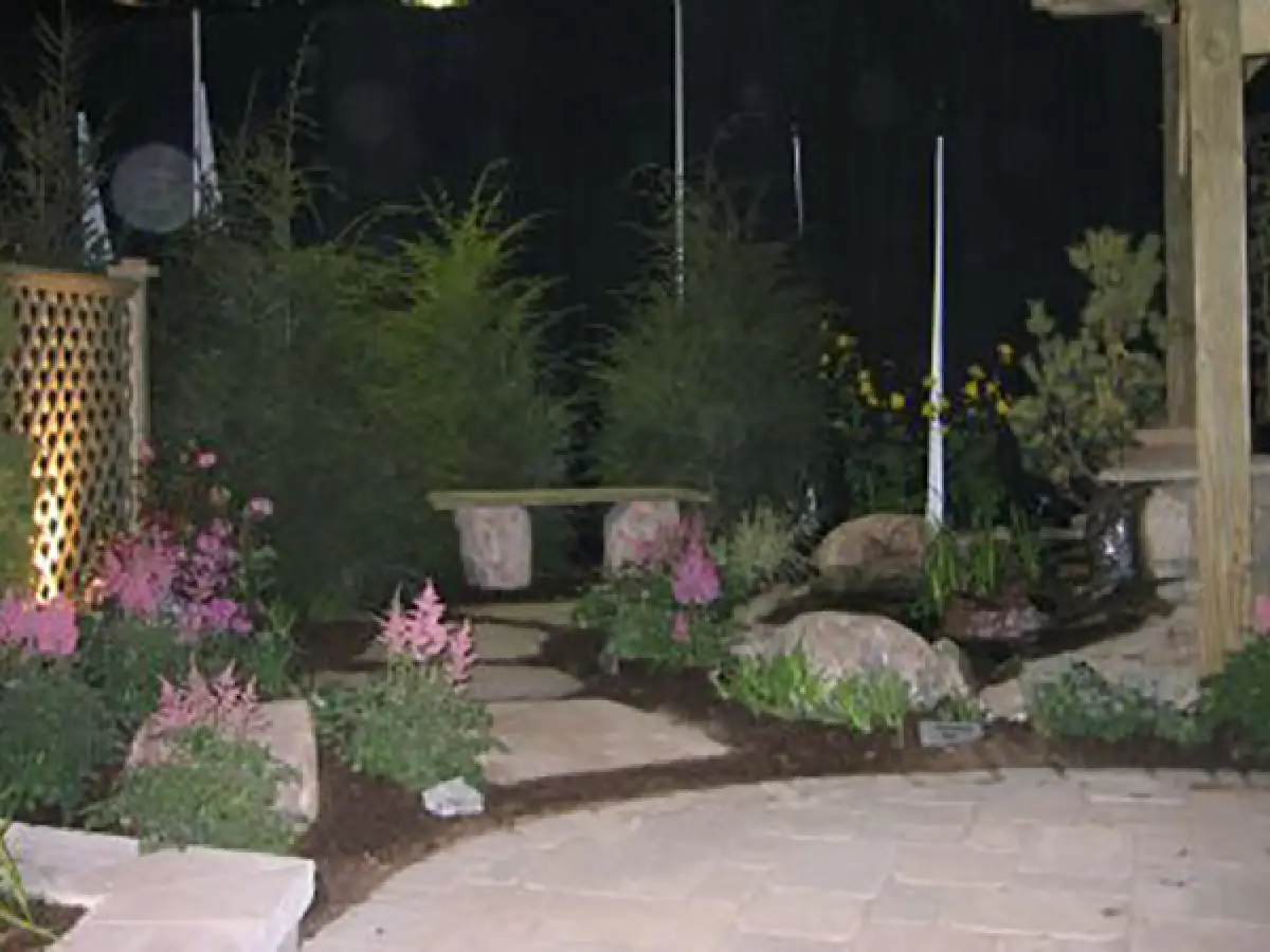 stone patio surrounded by mulch, stone work, stone bench, and a fence