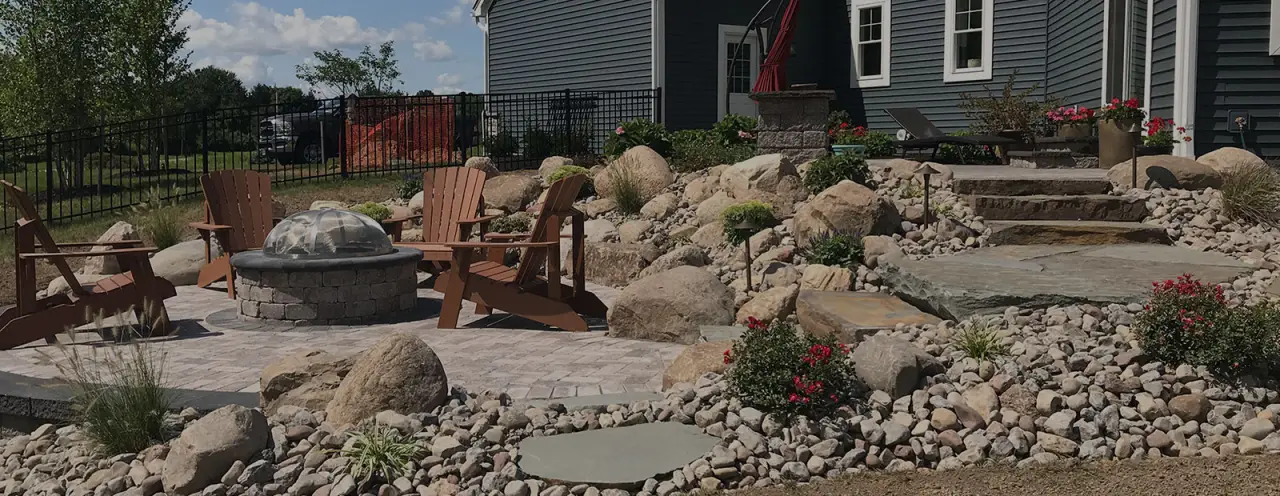 exterior of home with stone steps leading to stone patio with fire pit and wooden chairs
