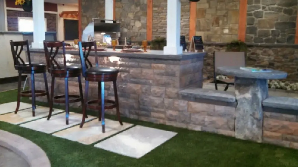 Stone outdoor kitchen with grill, bar seating, and patio chairs.