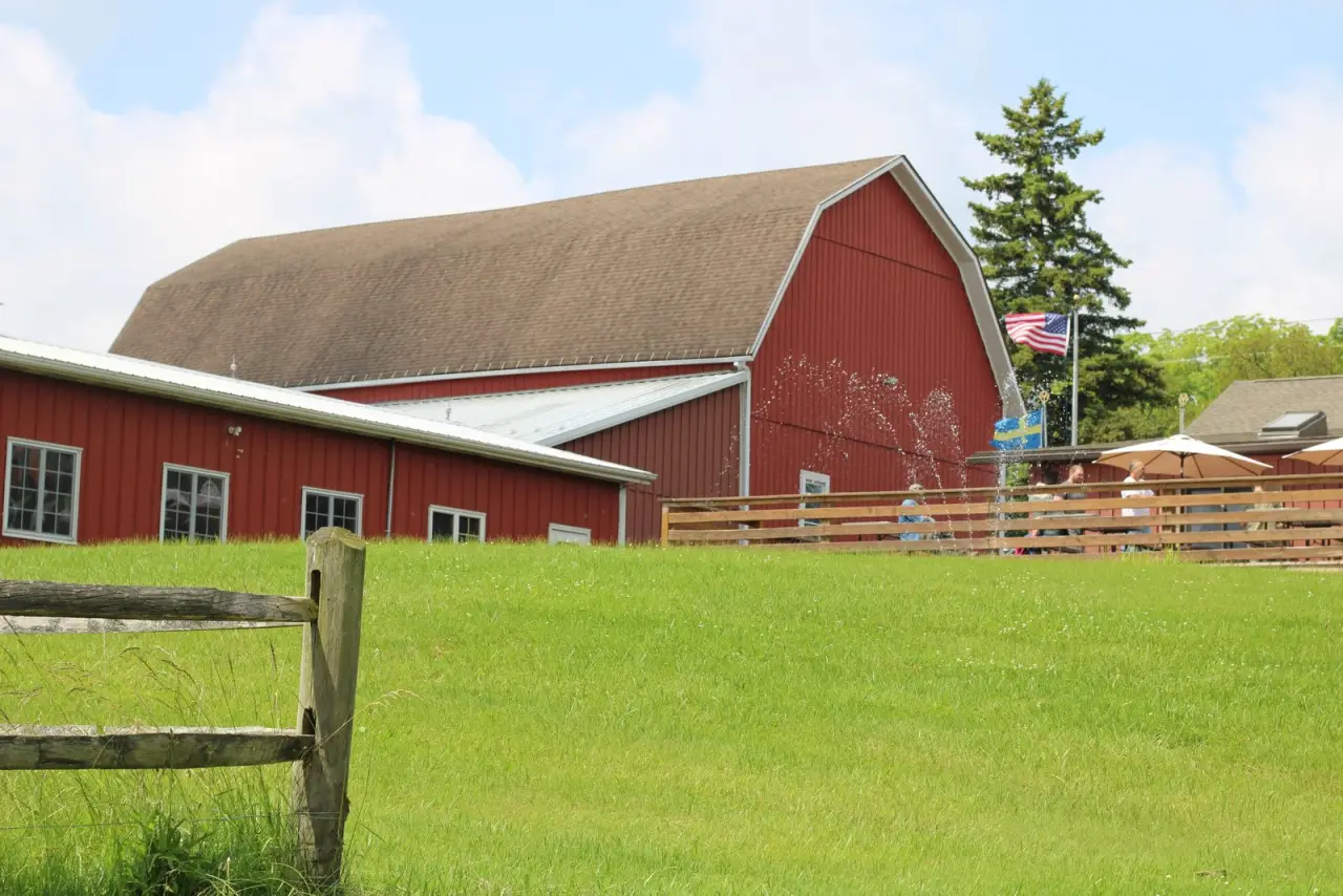 The red Swedish Hill barn beyond a split rail fence and lawn