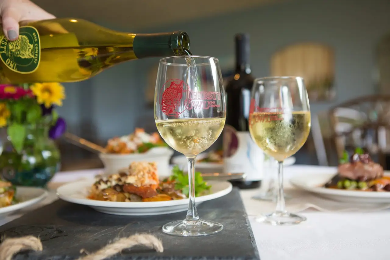 Wine being poured at a table set with lunch and glasses of white wine