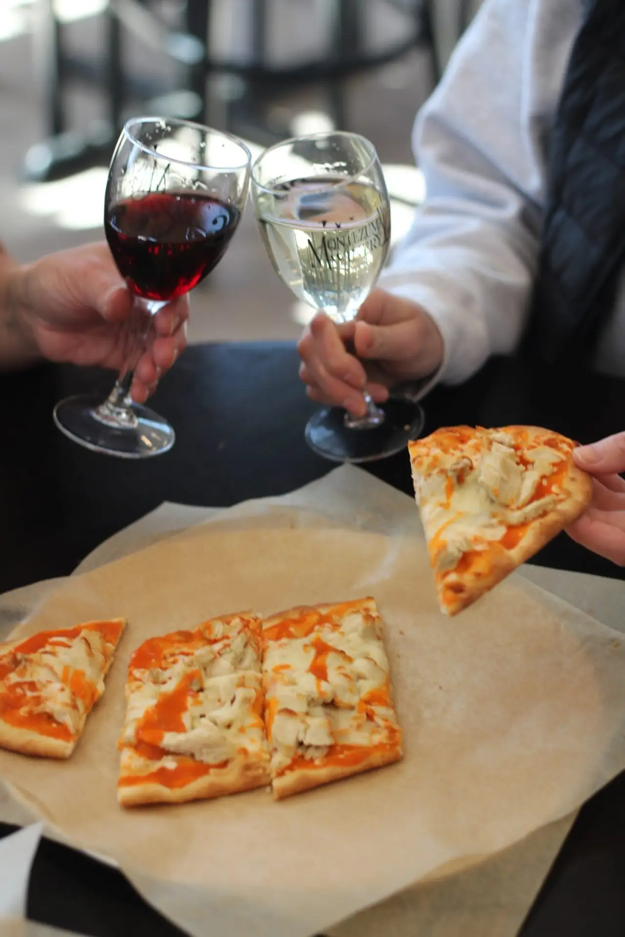 Two people toasting with wine over slices of naan pizza