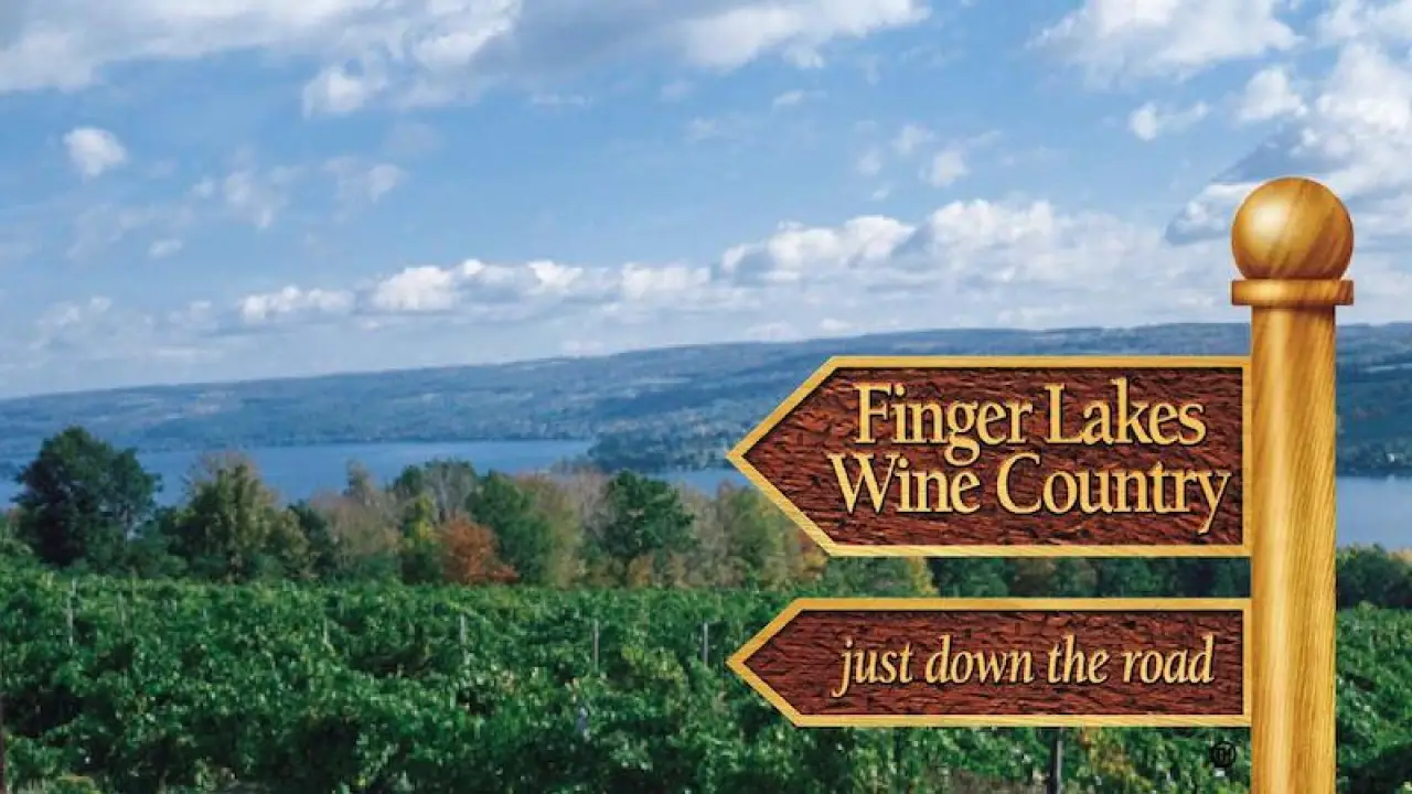Wooden sign points to Finger Lakes Wine Country with vineyards and a lake in the background.