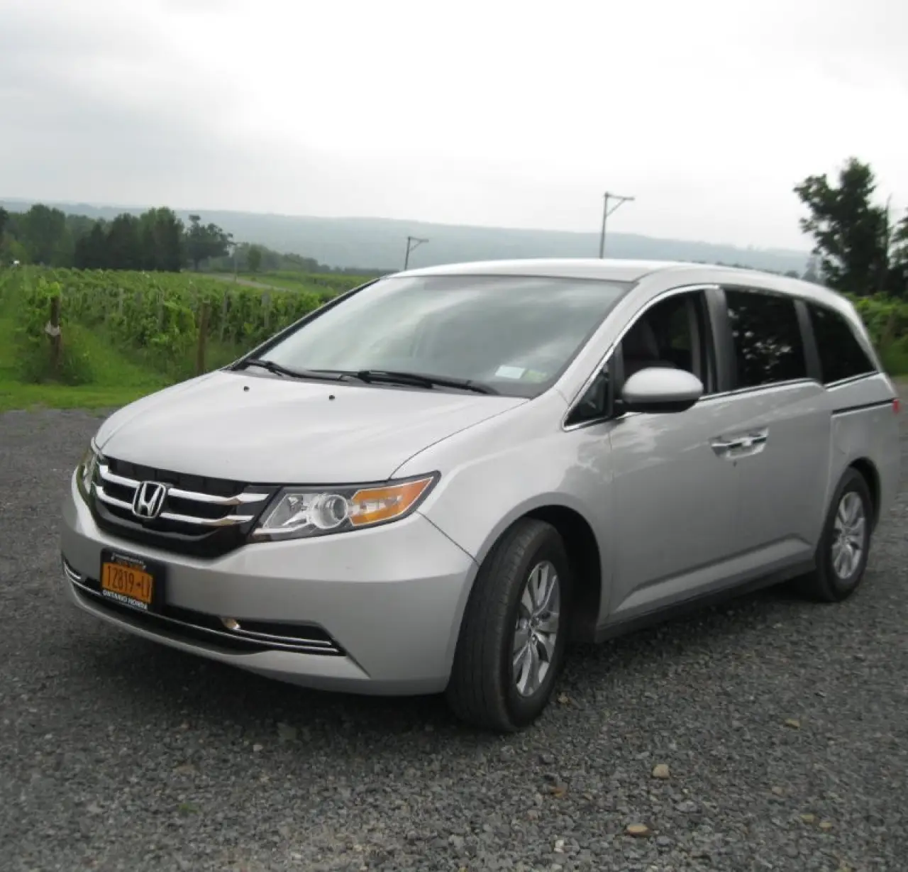 A silver Honda minivan parked on a gravel road with greenery in the background.