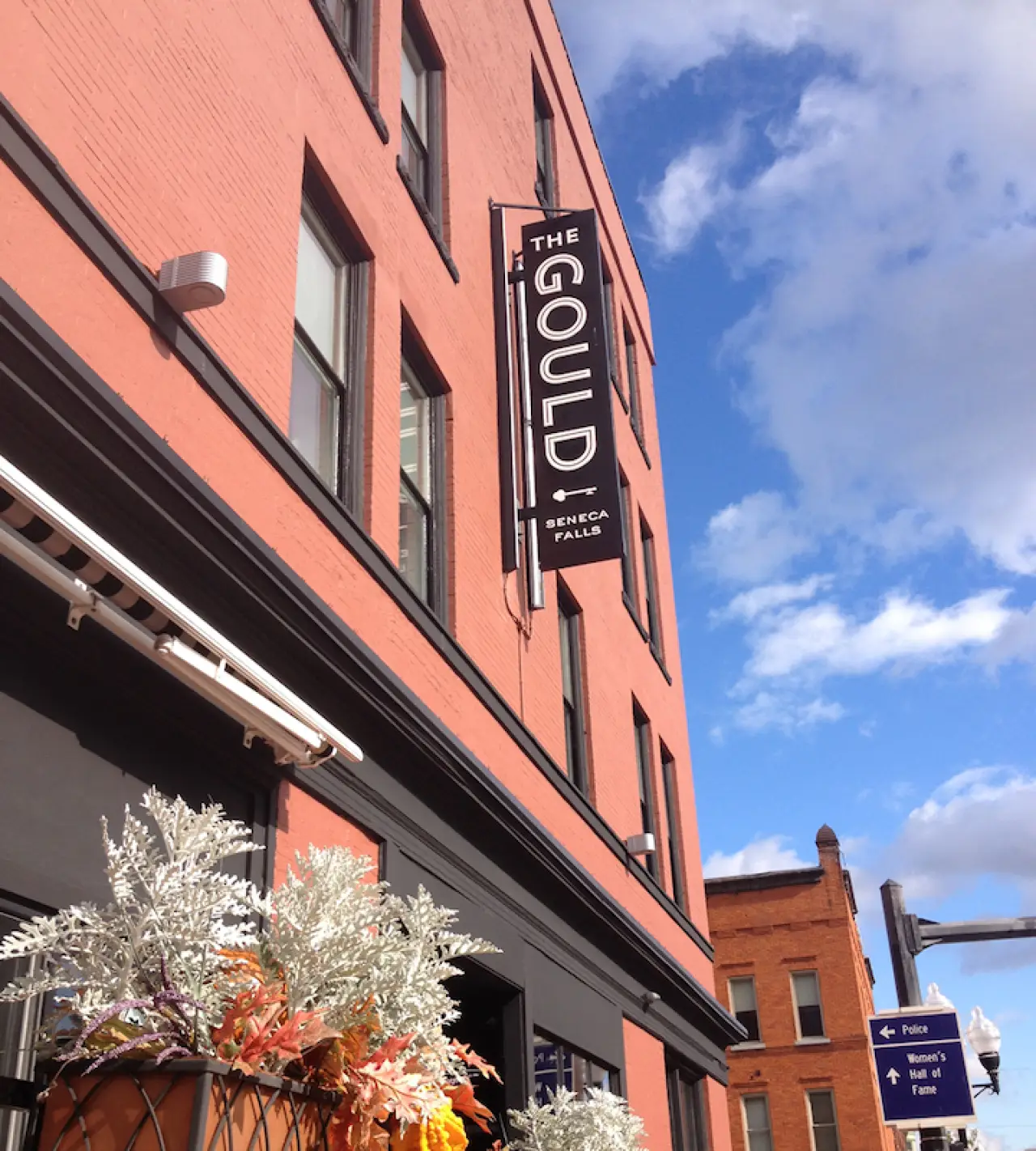 Red brick building with a “The Gould” sign, potted plants, and blue sky with clouds.