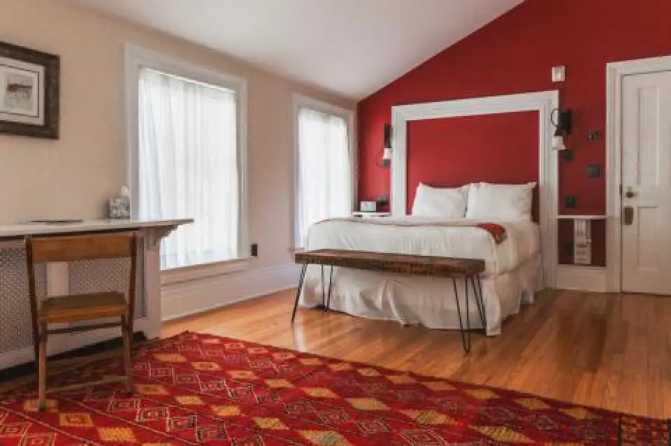 cozy bedroom with red accent wall bed, wooden desk, and patterned rug on hardwood floor