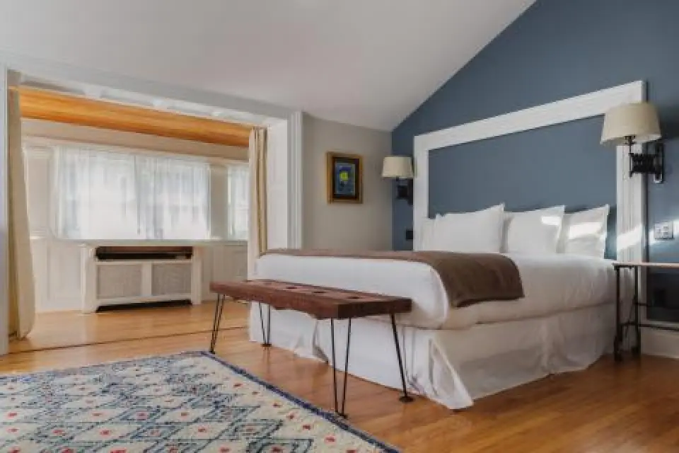 cozy bedroom with blue accent wall, double bed, wooden bench, rug, and bright window alcove
