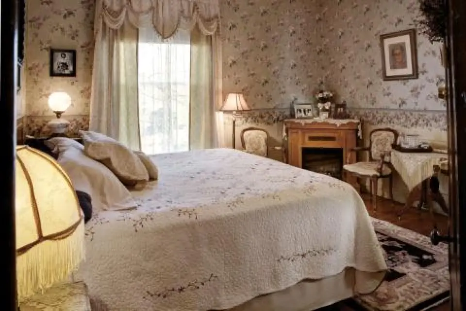 A vintage bedroom with floral wallpaper, a large bed, and antique-style furniture and lamps.