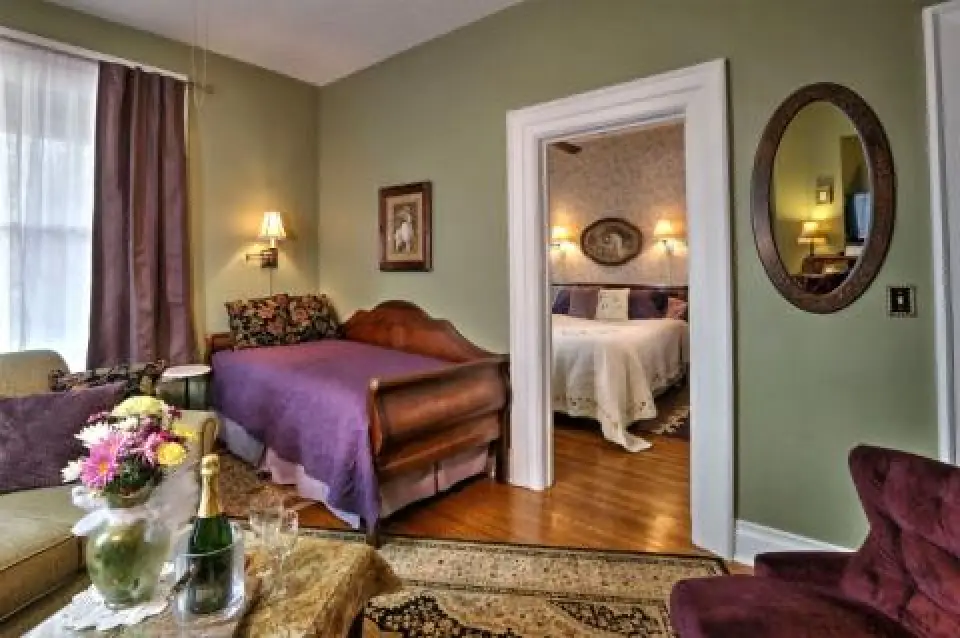 Cozy room with a daybed, purple bedding, flowers, and a view into a bedroom with a white bed.