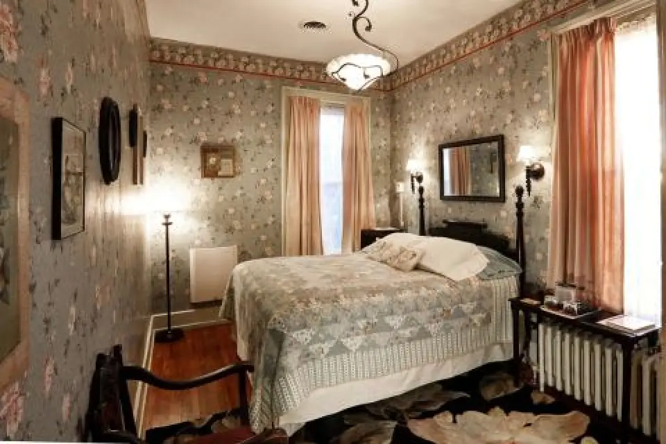 A vintage bedroom with floral wallpaper, a bed, soft lighting, and light pink curtains.
