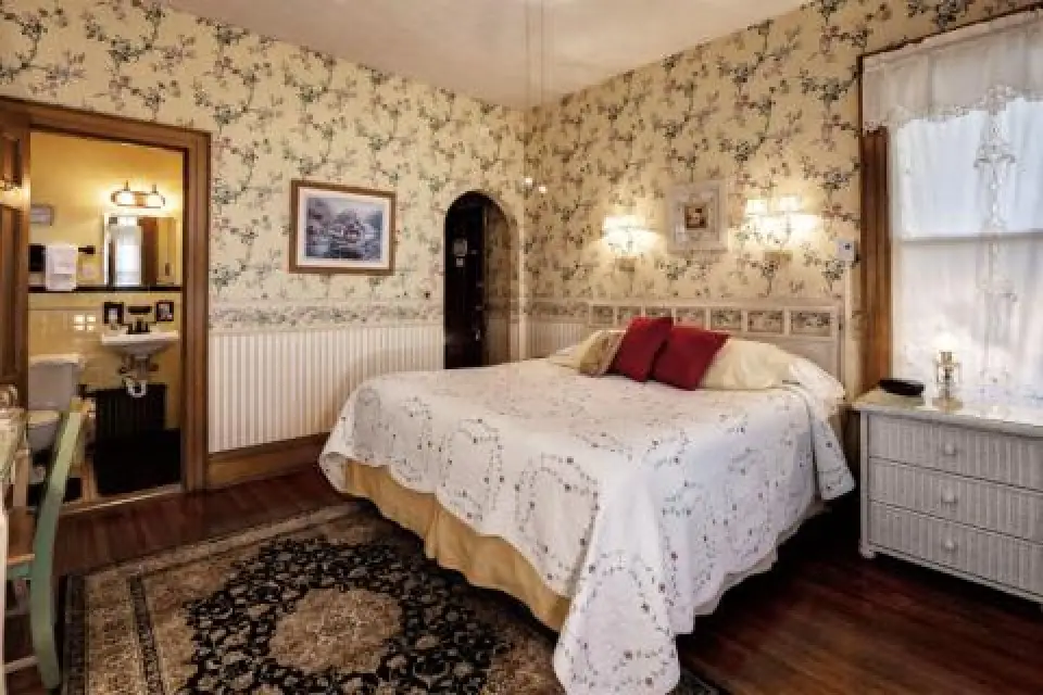 Cozy bedroom with floral wallpaper, a large bed, and vintage decor next to a small bathroom.