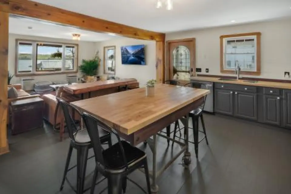 Open-plan kitchen and living area with wooden table, dark cabinets, sofas, and large windows.