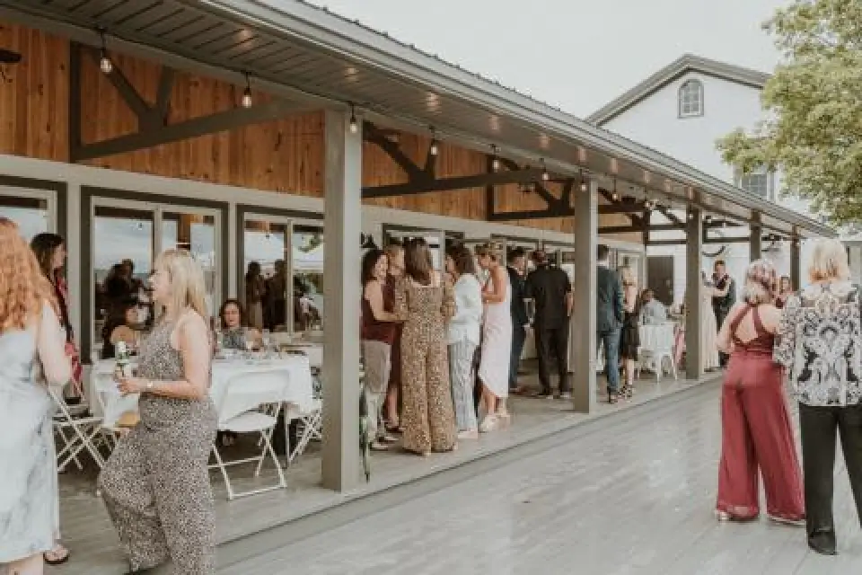 People gather, socialize, and dine at an outdoor covered patio during a daytime event.