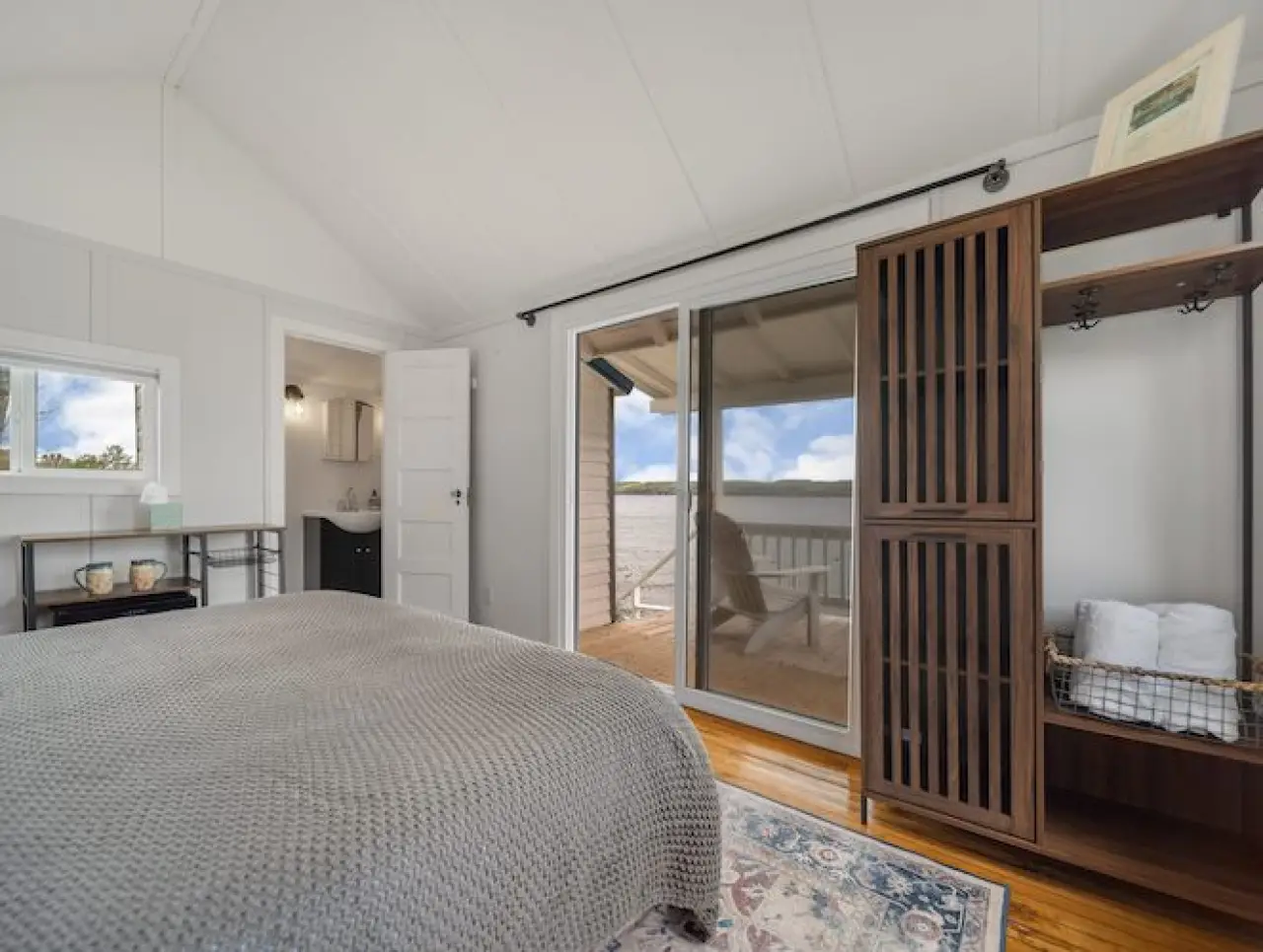 Bright bedroom with a gray bedspread, open closet, and sliding glass door to a lakeside deck.