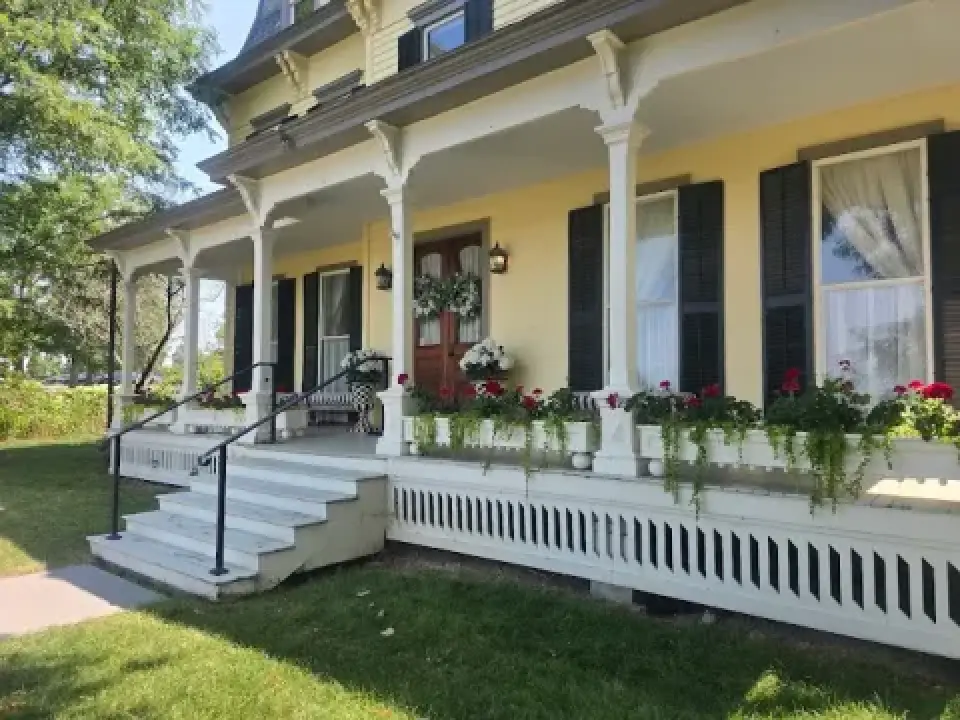 Yellow house with a wide porch, flower boxes, black shutters, and white railings.