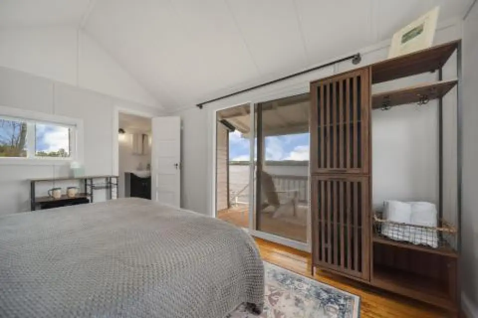 Bright bedroom with a bed, cabinet, and glass doors opening to a lake view balcony.