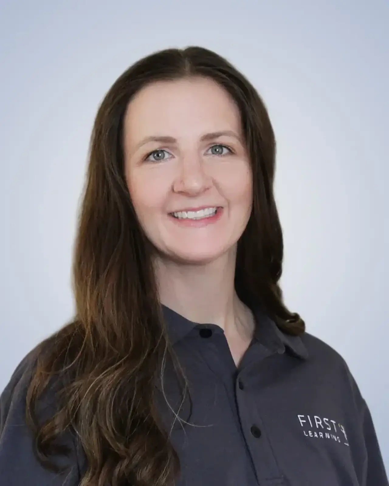 Woman with long brown hair in a dark polo shirt, smiling at the camera against a light background.