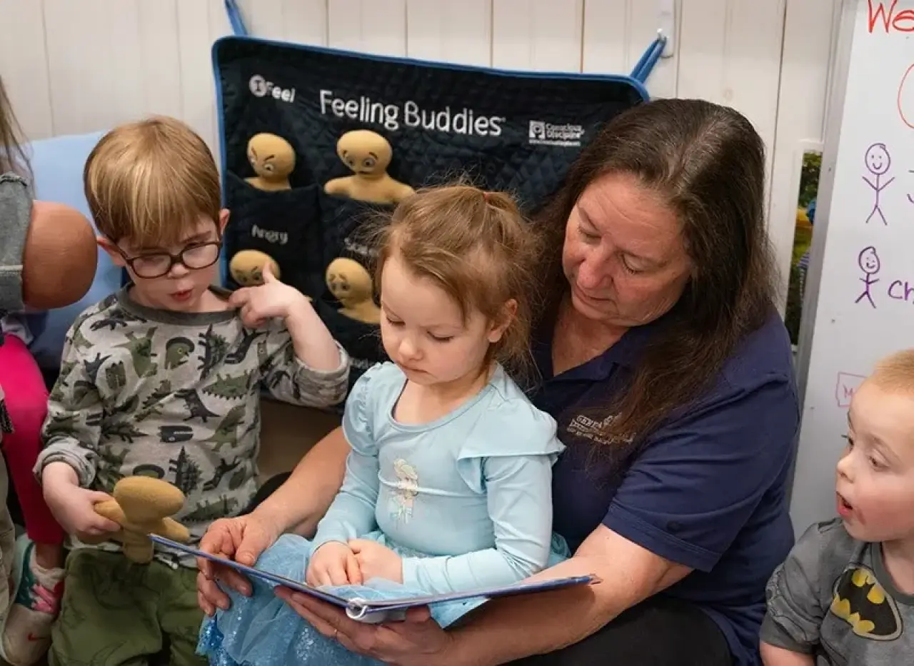 A preschool teacher with a child on their lap, reading a story to the kids.