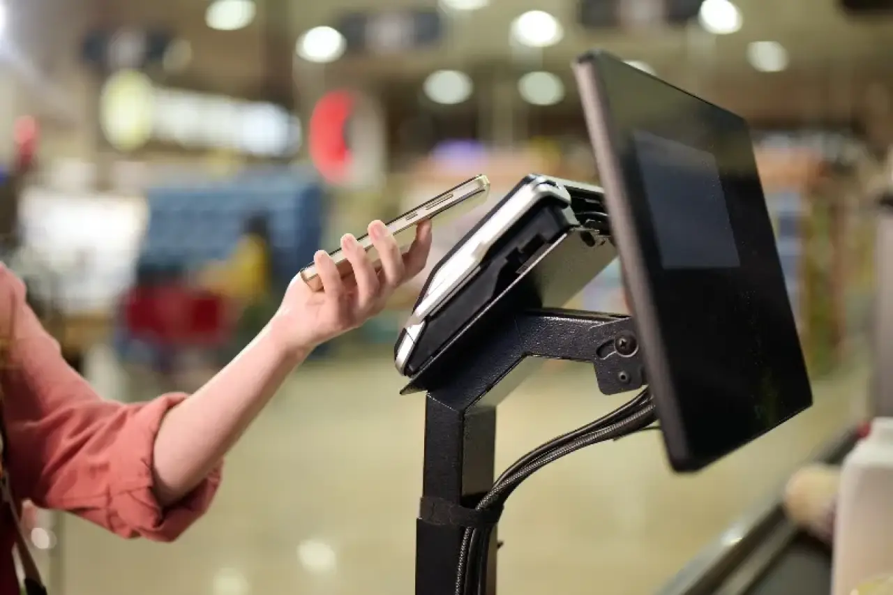Person paying with smartphone at a digital kiosk in a store.