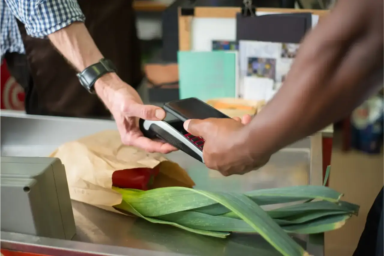 man uses tap-to-pay with his phone at a grocery to buy leeks and peppers