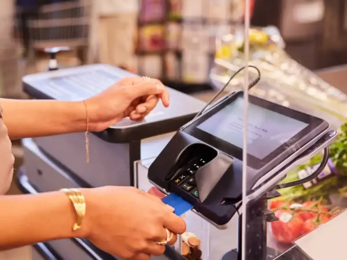 woman checking out at a grocery store with her blue credit card in the reader
